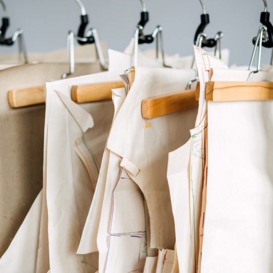 Many paper sewing patterns for different clothes hanging on the rack in sewing factory background. Clothing pattern, manufacture on sewing factory. Tailoring, small business Many paper sewing patterns for different clothes hanging on the rack in sewing factory background. Clothing pattern, manufacture on sewing factory. Tailoring, small business.